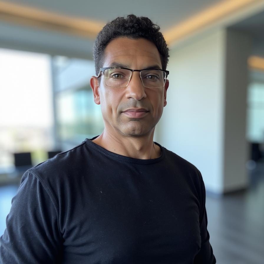 A person wearing a black shirt and glasses, posing indoors in a modern setting.