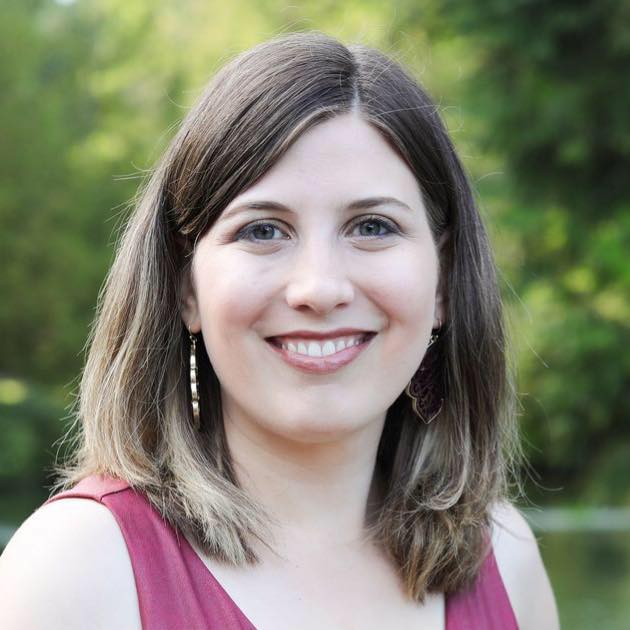 Portrait of a woman with medium-length brown hair, wearing a sleeveless top, smiling at the camera against a blurred green background.
